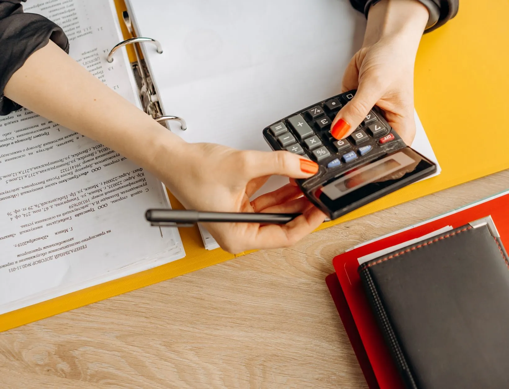 Hands checking figures on a calculator over an open ring binder of invoices
