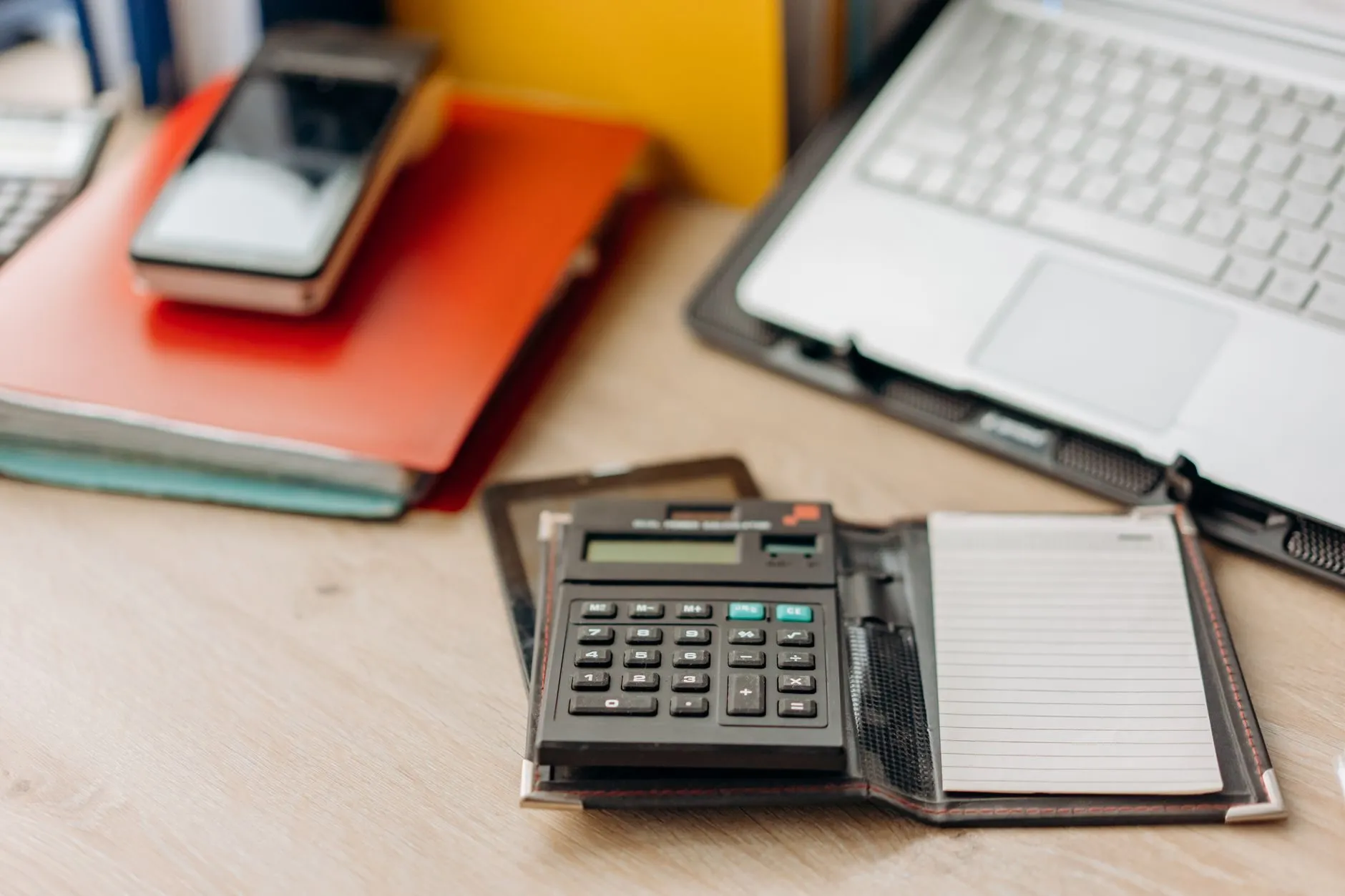 A calculator in a leather notepad holder beside a laptop