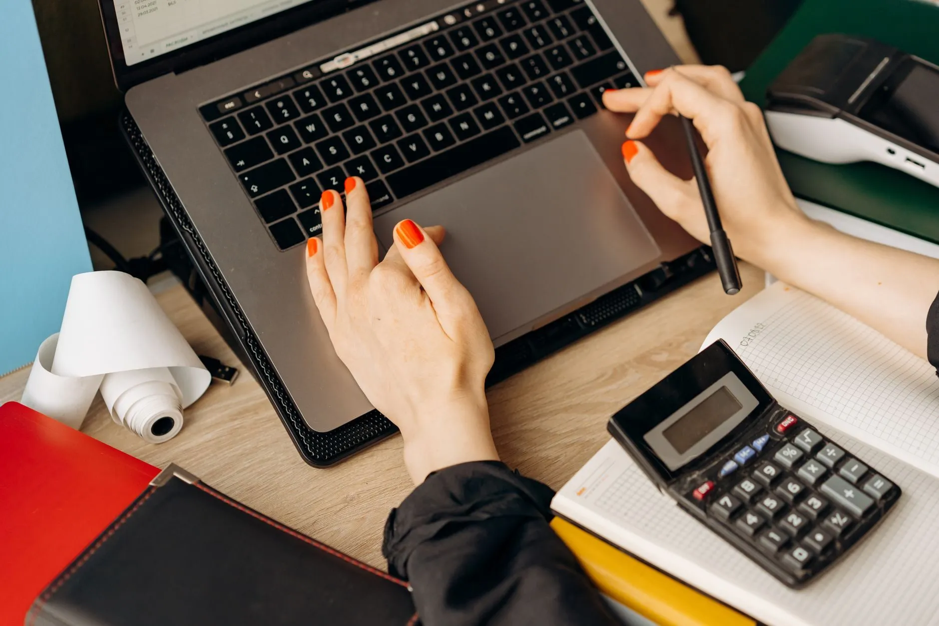 Hands on a laptop trackpad beside a calculator and a notebook