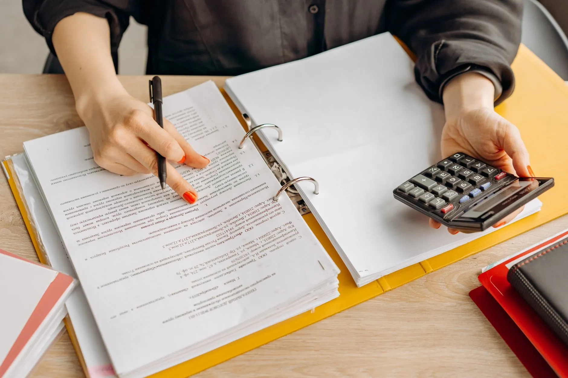 Hands marking a printed return in a yellow ring binder while holding a calculator